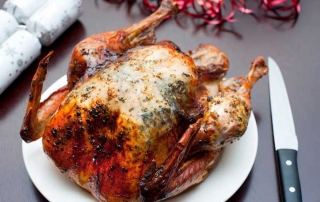 Whole roast Christmas turkey served ready on a plate for carving alongside festive crackers and table decorations