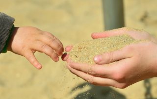 Photo of a woman's cupped hands passing sand to a child